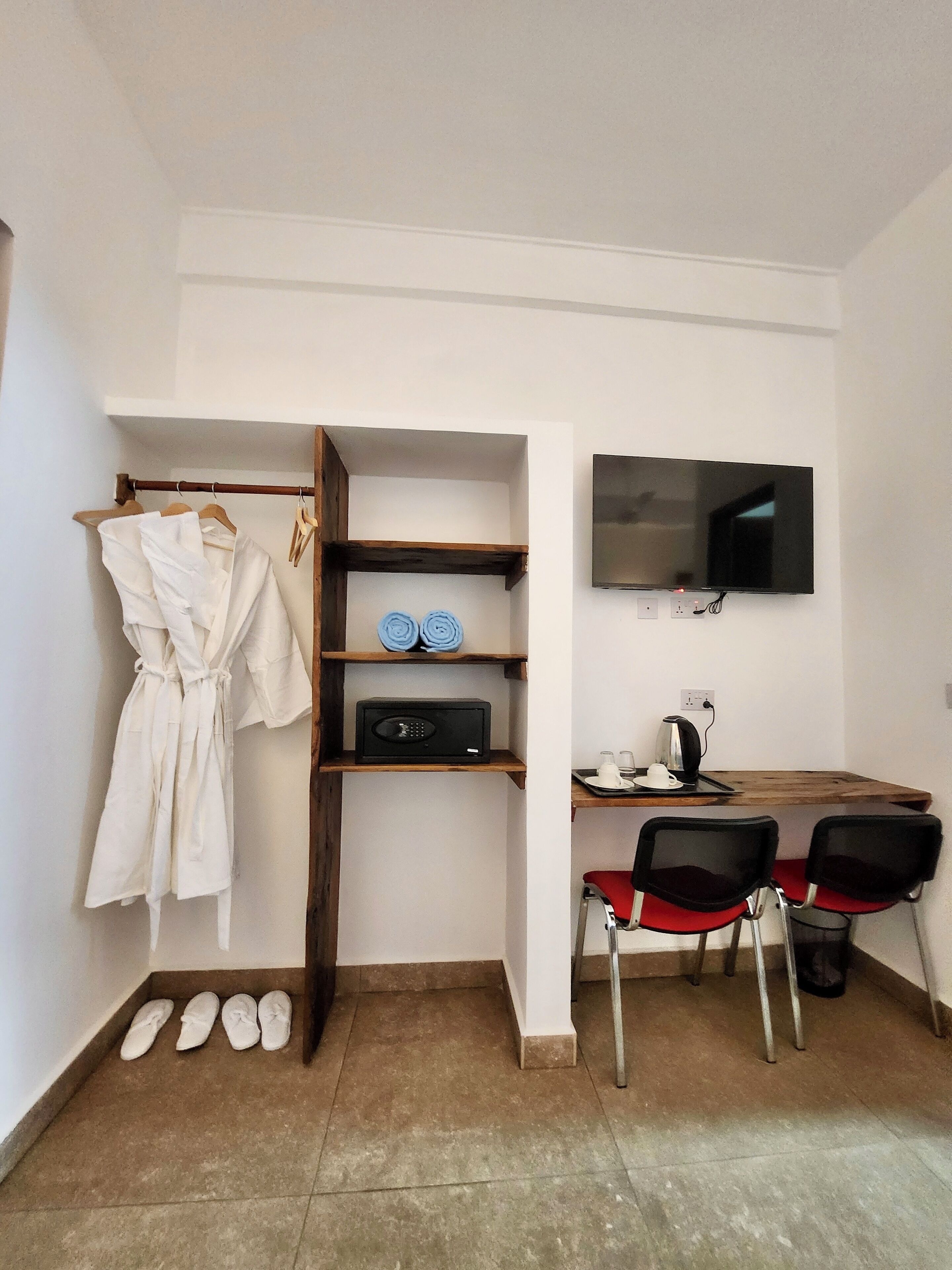 Ein Zimmer mit einem Bett, einem Schreibtisch mit Stuhl, einem Fernseher, einer Mikrowelle und einem Bademantel, der an einem Gestell hängt.