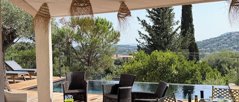 Un área de comedor al aire libre con mobiliario de mimbre, una piscina y vistas del paisaje.