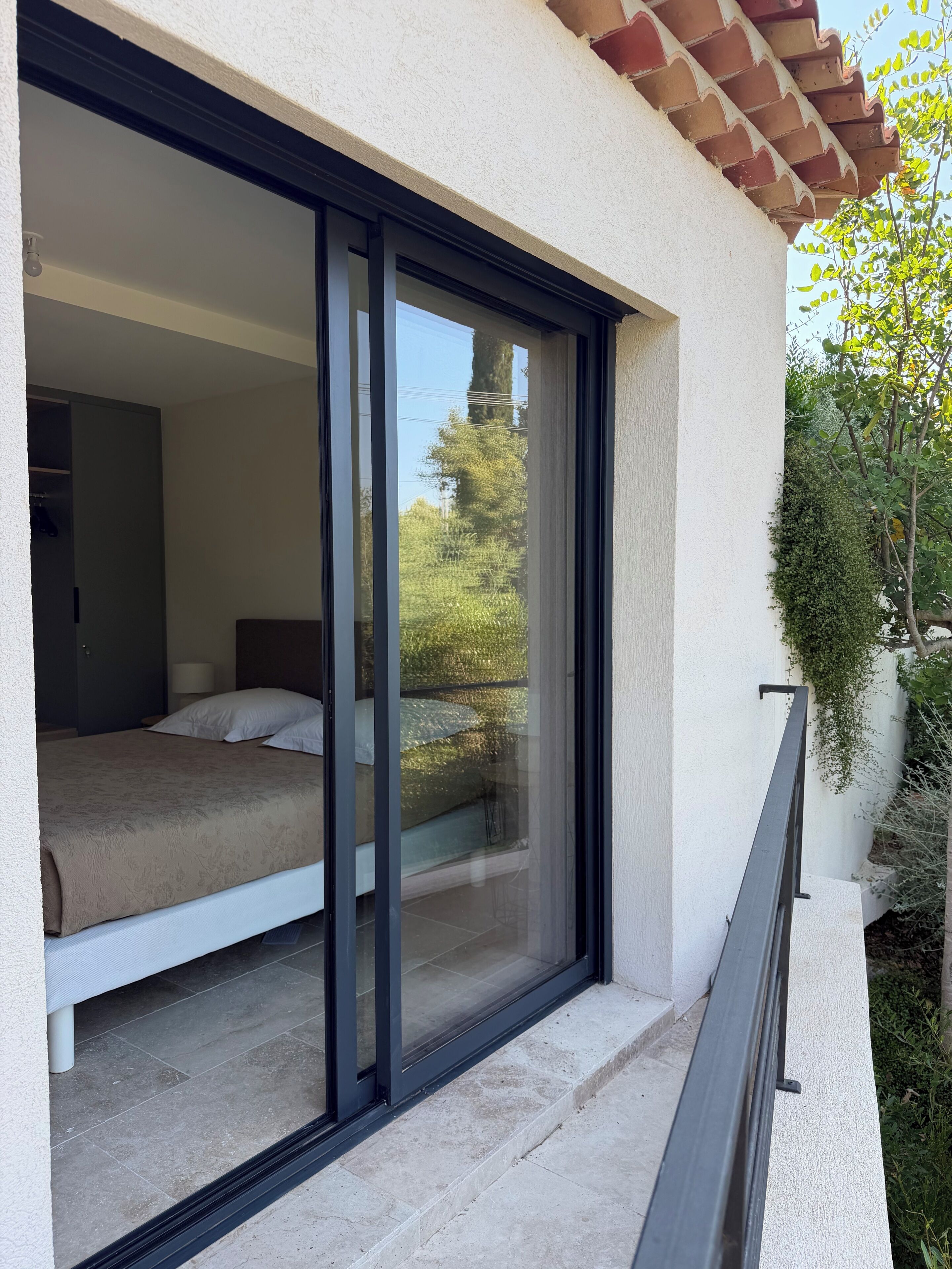 A bedroom with a bed, a sliding glass door, and a view of greenery outside.