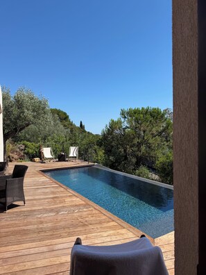 Eine Holzterrasse mit Pool, Liegestühlen und Blick auf Bäume und Hügel.