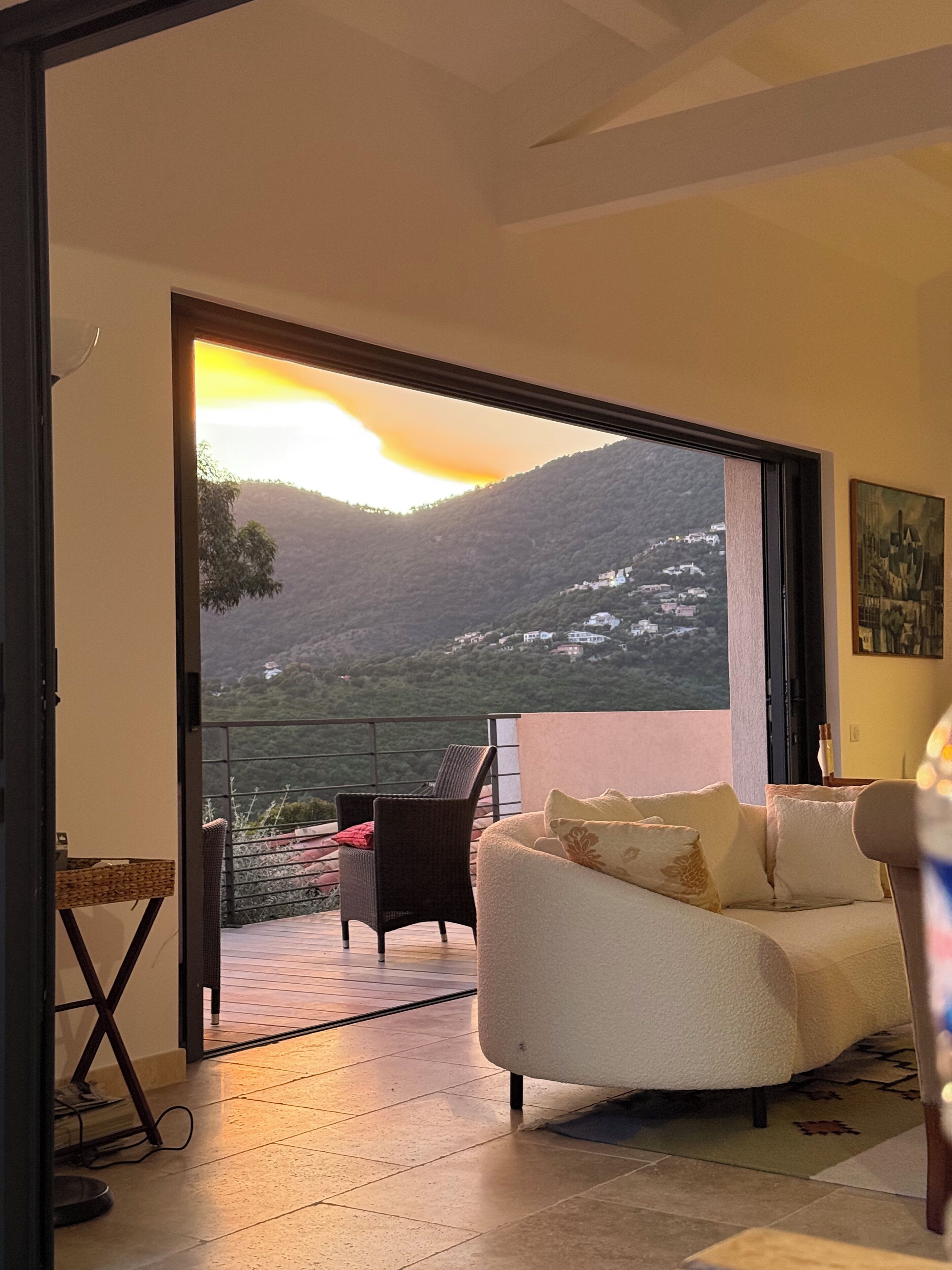 Une pièce comprenant un canapé, un fauteuil et offrant une vue sur un paysage montagneux par une porte ouverte.