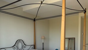Ein Bett mit Baldachin, eine Bettdecke mit Muster, ein Nachttisch mit Lampe und ein Spiegel an der Wand.
