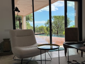 A room with a large window, a pool, and two chairs. - NEW CHARMING VILLA WITH POOL, SEA VIEWS, AND HILLS, 1 KM FROM THE BEACH (Cavalaire-sur-Mer)