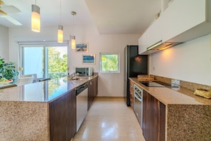 A modern kitchen with granite countertops, a central island, a built-in oven, and a large window providing natural light. - Luxury apartment with pool & high speed WIFI (Playa del Carmen)