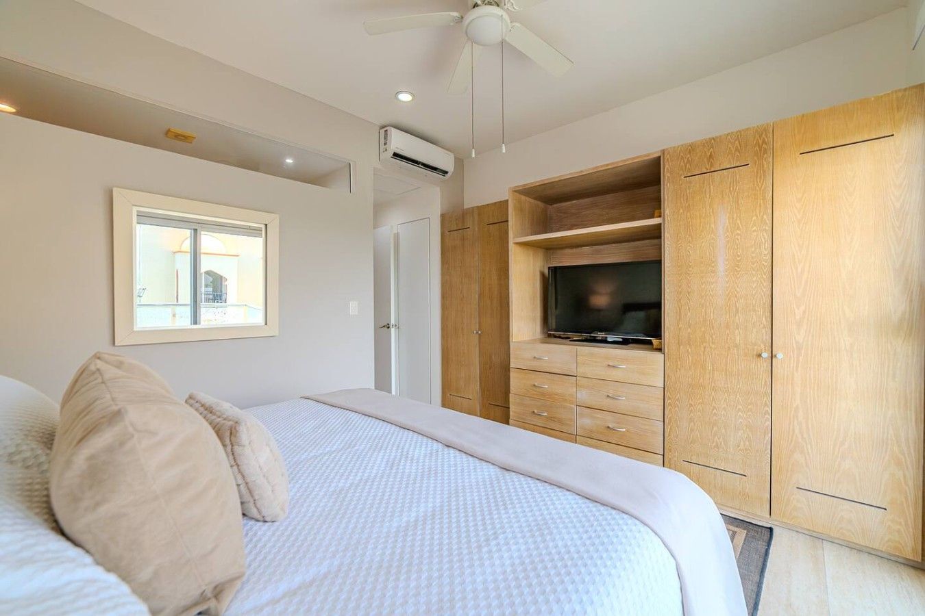 Een slaapkamer met een bed, een televisie op een houten kast en een plafondventilator.
