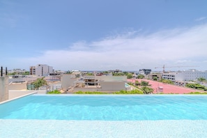 A rooftop pool with a view of a cityscape, including buildings and a distant shoreline. - Luxury apartment with pool & high speed WIFI (Playa del Carmen)