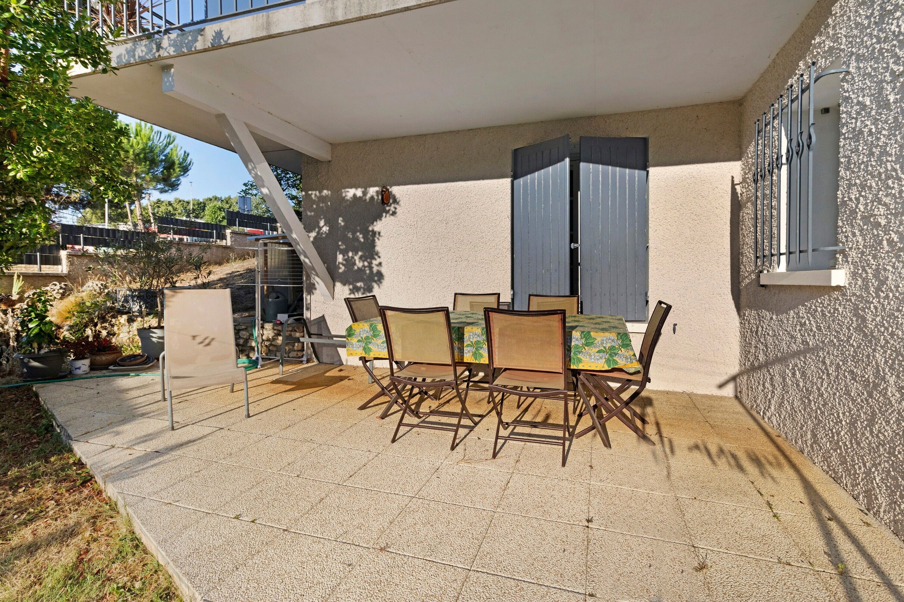 An outdoor patio with a table and chairs, a covered seating area, and a view of a building with a balcony.