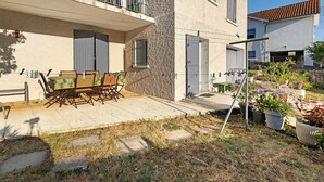 A courtyard with a dining table and chairs, a small garden with potted plants, and a building with a balcony.