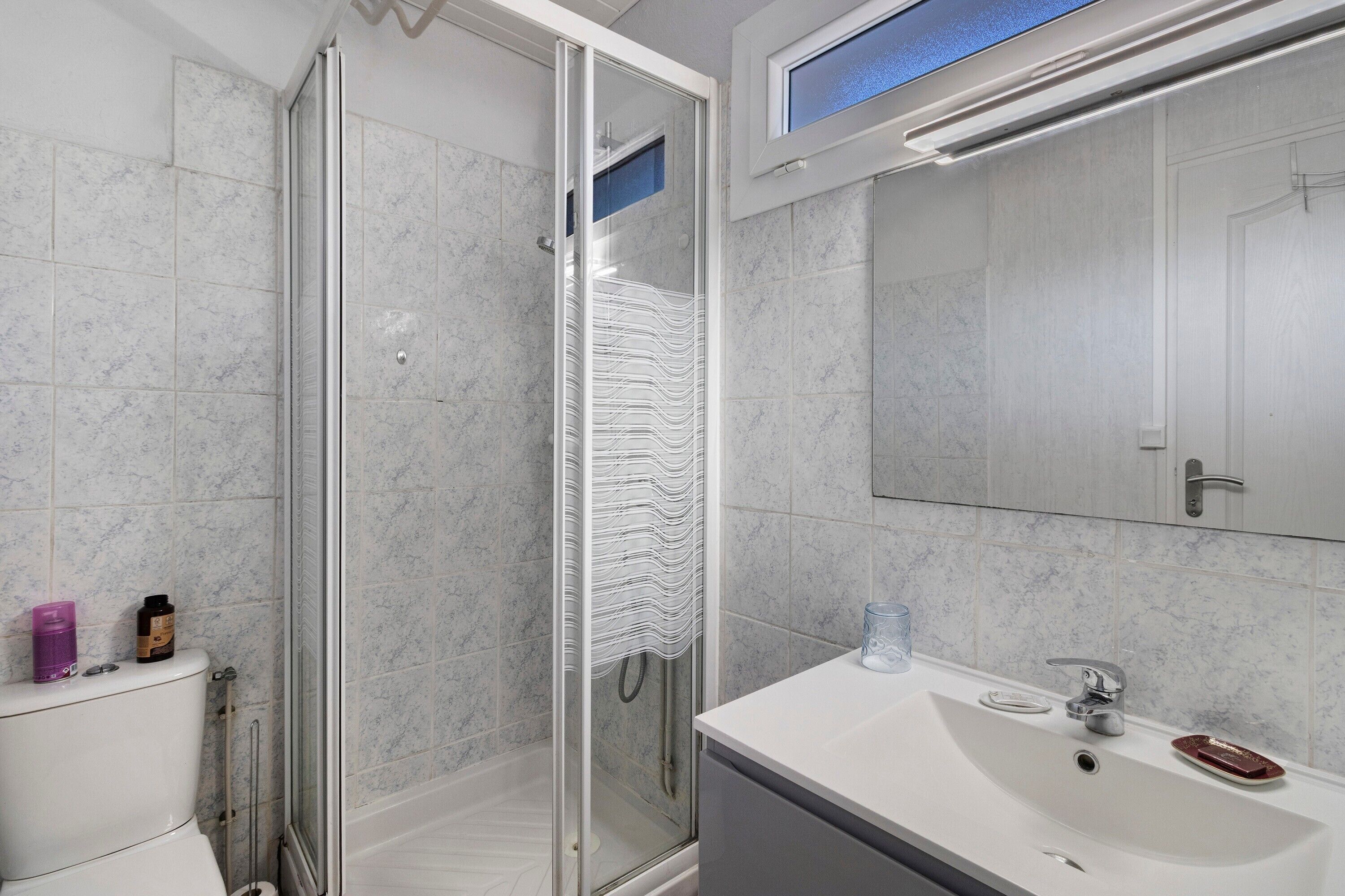 Un bany modern amb plat de dutxa de vidre, un lavabo blanc i un mirall sobre el lavabo.