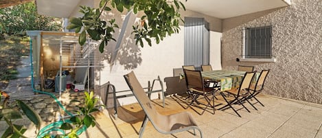 Une terrasse extérieure avec une table et des chaises, entourée de plantes et d’une structure métallique.