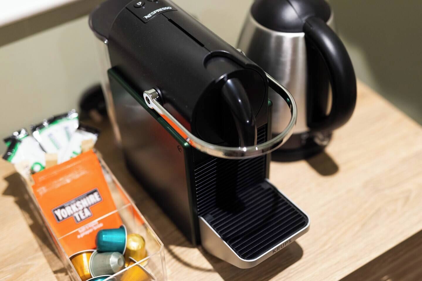 Uma máquina de café com vaporizador de leite, uma chaleira e uma caixa de chá Yorkshire sobre uma superfície de madeira.