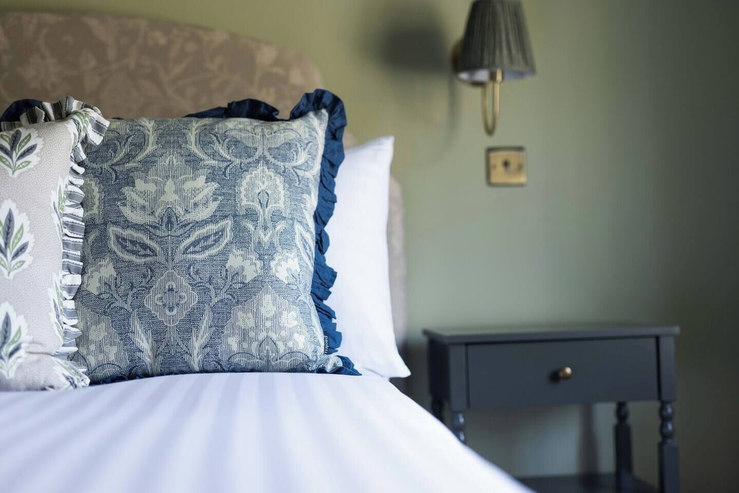 A bed with patterned pillows, a bedside table, and a wall-mounted lamp.