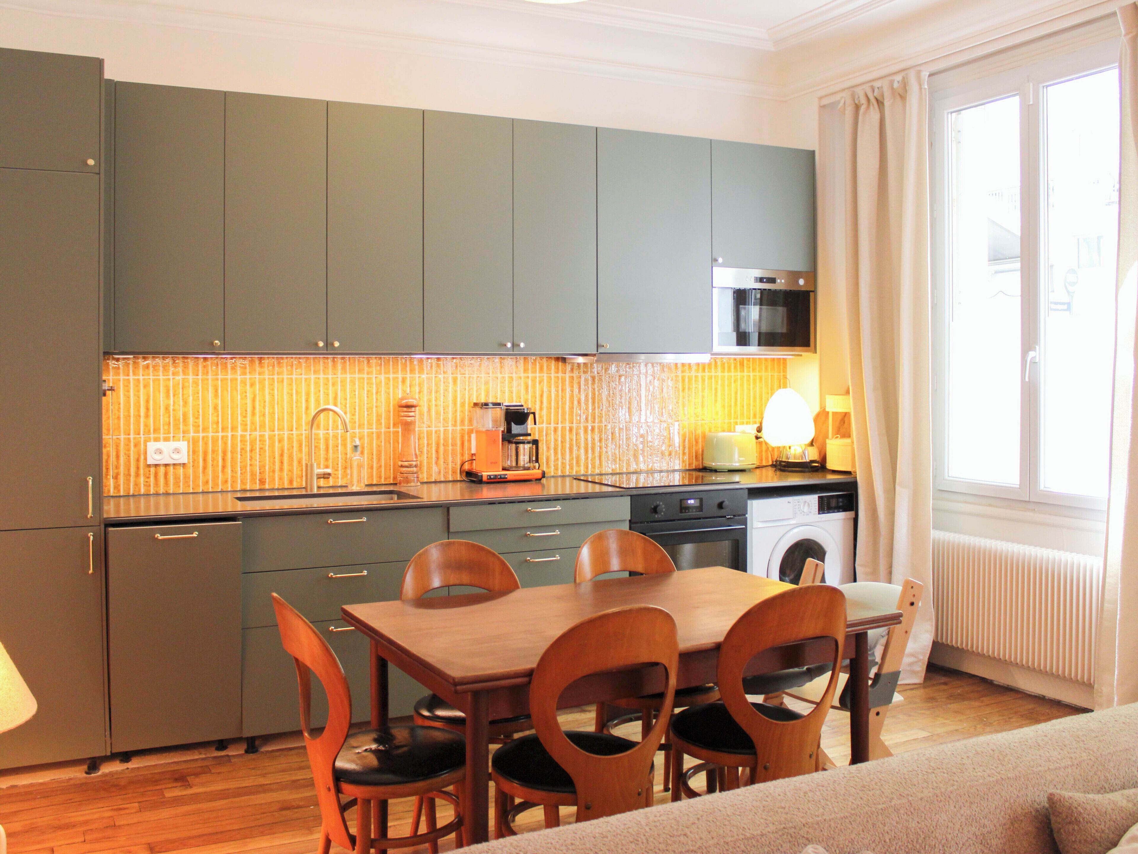 A compact kitchen with a dining area, a washing machine, and a window with curtains.