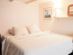 Quarto com cama, almofadas, luminária na parede e quadro emoldurado.