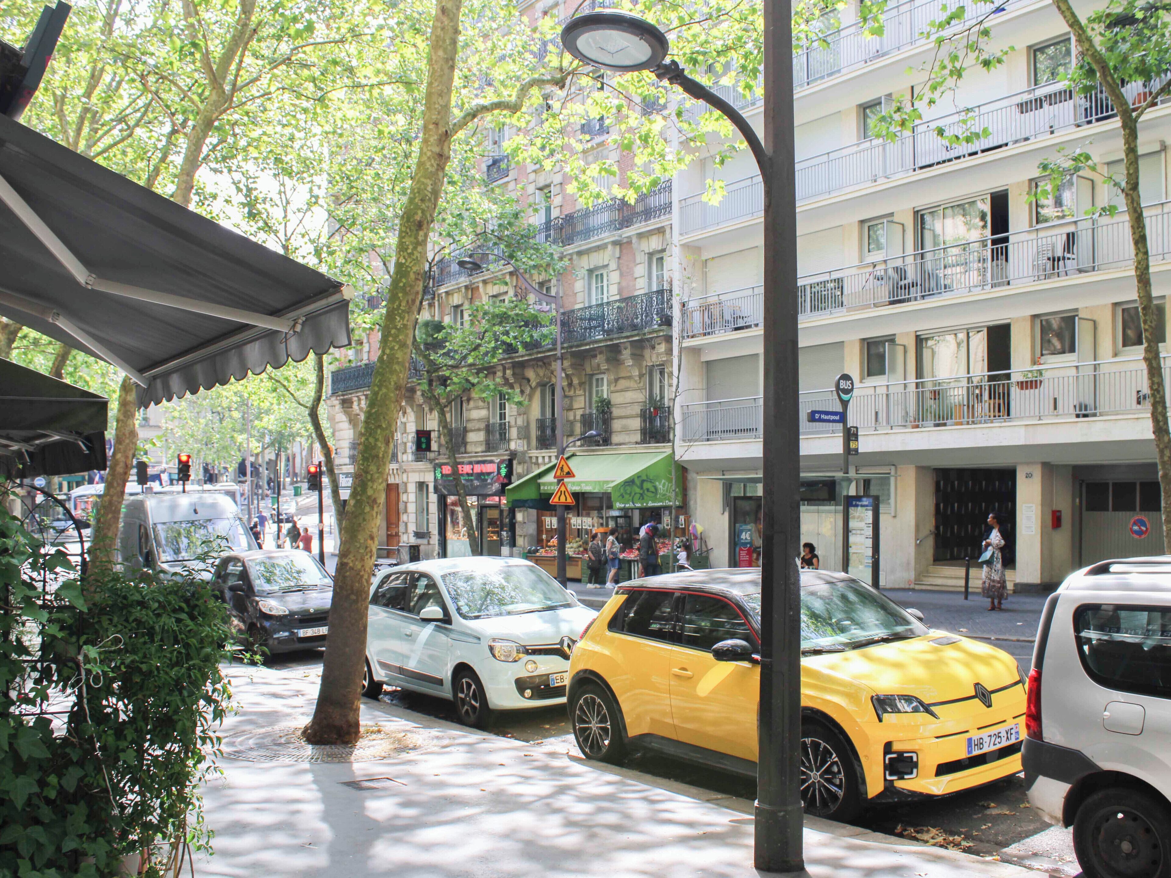 A street scene with parked cars, trees, and a building with balconies.