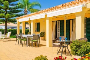Eine überdachte Terrasse mit Esstisch und Stühlen, ein kleiner runder Tisch mit zwei Stühlen und ein Blumentopf.