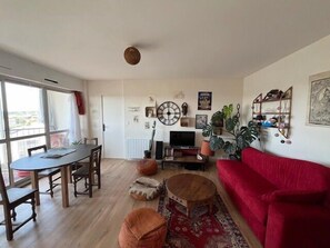 A living room with a red sofa, a wooden dining table, and a television. - Bright apartment with balcony in Vannes (Vannes)
