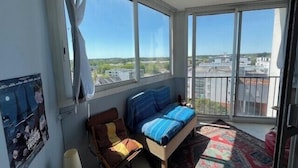 Uma varanda com uma cama, uma cadeira e vista para a cidade.