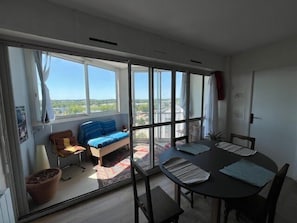 A room with a large sliding glass door leading to a balcony, a round dining table with chairs, a sofa, and a potted plant. - Bright apartment with balcony in Vannes (Vannes)