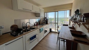 Cozinha moderna com armários brancos, bancada de madeira e uma janela ampla com vista para a cidade.