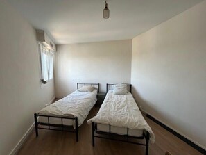A small, single-room accommodation with two single beds, a window with curtains, and a light fixture. - Bright apartment with balcony in Vannes (Vannes)