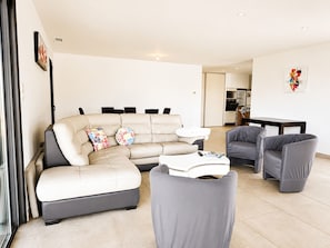 A modern living room with a sectional sofa, two armchairs, a coffee table, and a dining area with a table and chairs. - Spacious house with sea and mountain views (BASTELICACCIA)
