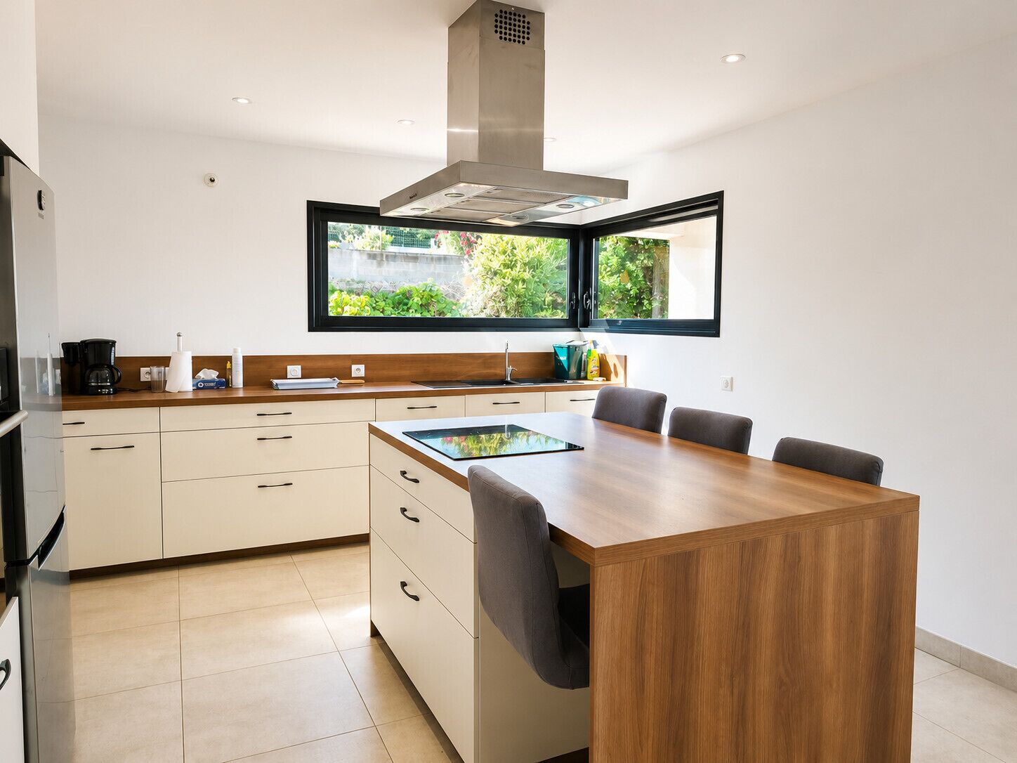 A modern kitchen with a central island, a built-in stove, and a window overlooking greenery.