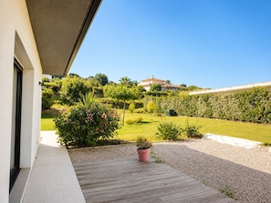 A modern building with a wooden deck, a garden with various plants, and a clear blue sky. - Spacious house with sea and mountain views (BASTELICACCIA)
