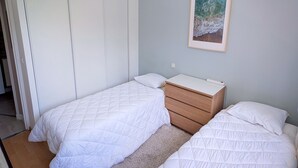 Een slaapkamer met twee bedden, een nachtkastje, een dressoir, een plafondlamp en een ingelijst schilderij aan de muur.