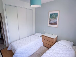 Ein Schlafzimmer mit zwei Betten, einem Nachttisch, einer Kommode, einer Deckenleuchte und einem gerahmten Bild an der Wand.