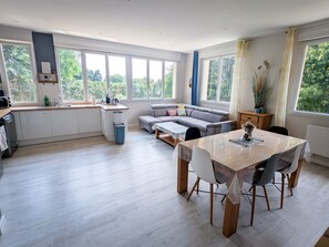 A modern kitchen with a dining area, large windows, and a grey sofa. - Pleurtuit, a luminous green haven (Pleurtuit)