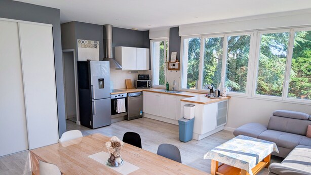 Een moderne keuken met een koelkast, oven en magnetron. Er is een eettafel met stoelen en een bank in de woonkamer.