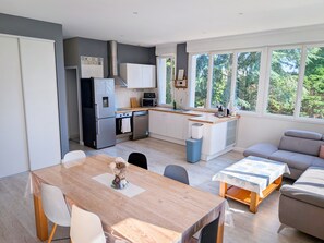 Cuisine moderne équipée d’un réfrigérateur, d’un four et d’un four à micro-ondes. On y trouve une table à manger avec des chaises, ainsi qu’un canapé dans l’espace salon.
