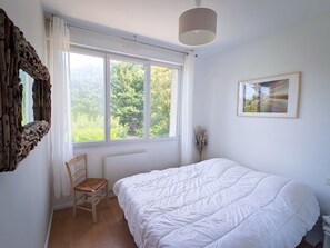 A bedroom with a large window, a bed, a chair, a radiator, and a framed picture on the wall. - Pleurtuit, a luminous green haven (Pleurtuit)