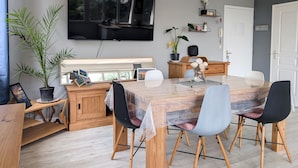 Een moderne eethoek met een houten tafel, stoelen, een aan de muur bevestigde televisie en een potplant.