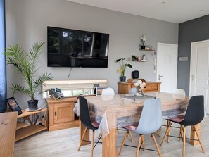 Ein moderner Essbereich mit Holztisch, Stühlen, einem an der Wand montierten Fernseher und einer Topfpflanze.