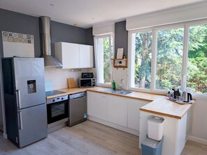 A modern kitchen with a stainless steel refrigerator, a microwave, and a dishwasher. There is a window providing a view of the outdoors.