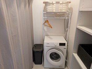 Ein kleiner Waschraum mit einer Waschmaschine mit Frontlader, einem Wäscheständer und einem Wäschekorb.