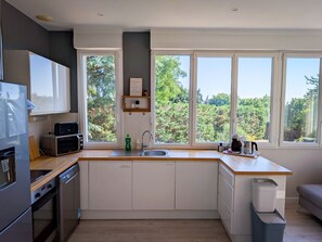 Une cuisine moderne équipée d’un four à micro-ondes encastré, d’un évier et d’une fenêtre donnant sur une forêt.