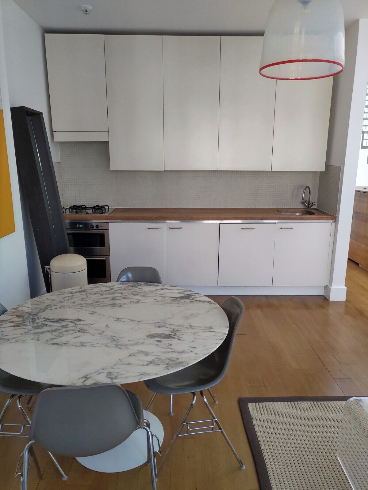 Une cuisine moderne avec des meubles blancs, un plan de travail en marbre et une table de salle à manger ronde, assortie de chaises.