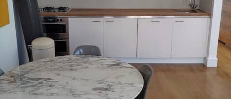 Una cocina moderna con armarios blancos, encimera de mármol y una mesa redonda con sillas.