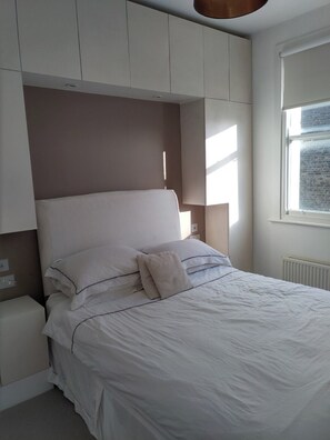Ein Schlafzimmer mit einem Bett, Nachttischen, einem Fenster und eingebauten Schränken.
