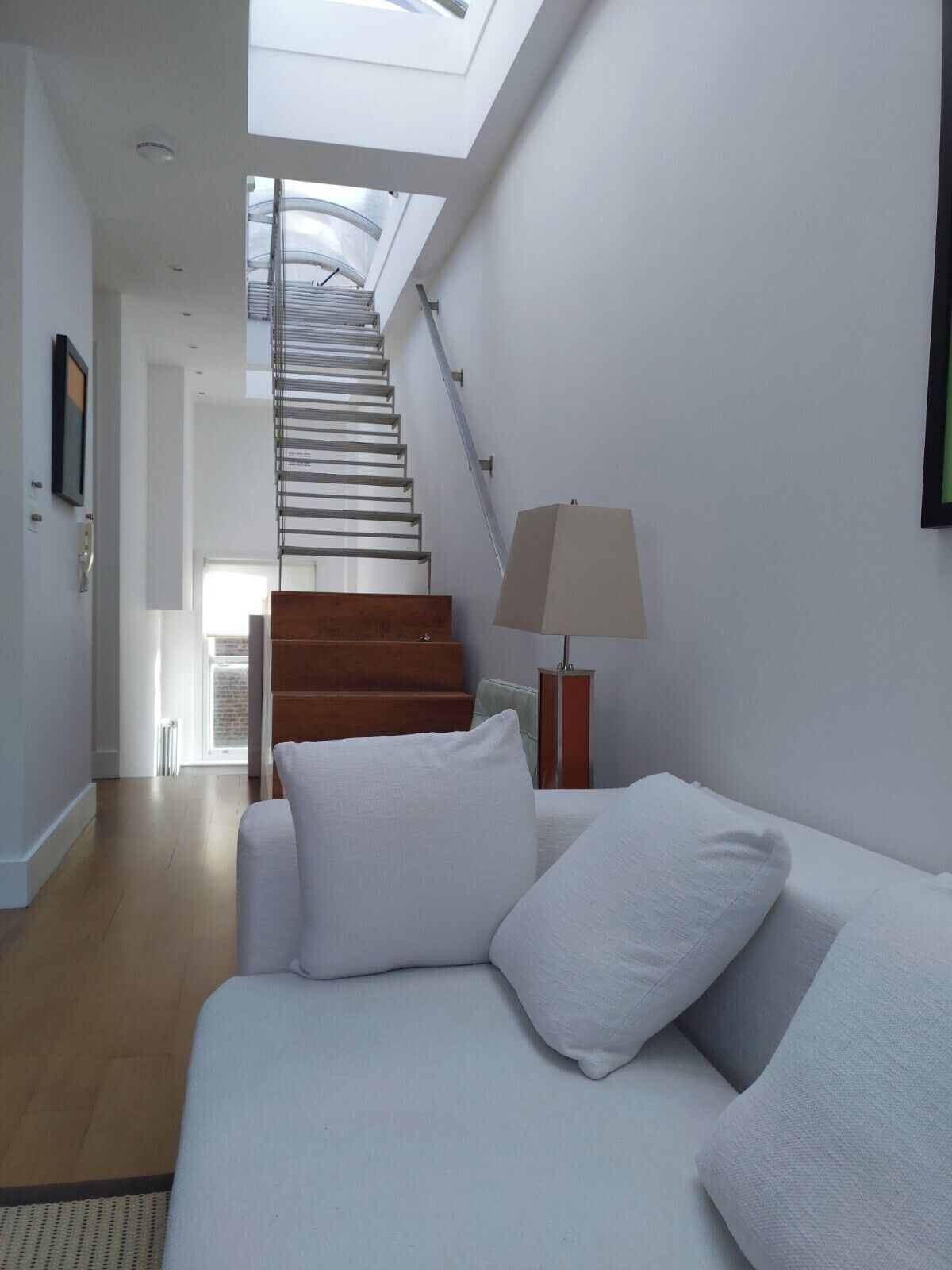 A modern interior with a staircase leading to a skylight, a sofa with cushions, and a floor lamp.