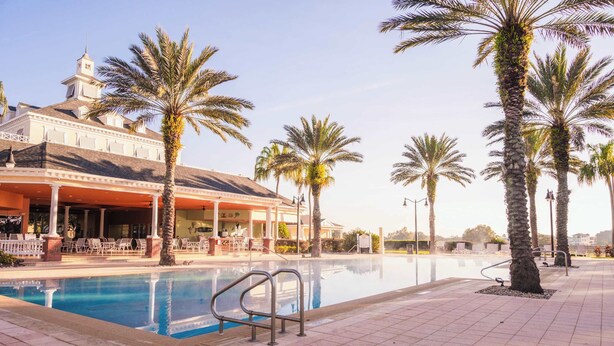 A pool area with palm trees, a covered seating area, and a building with a tower. - New! Epic Reunion Family Retreat (Kissimmee)