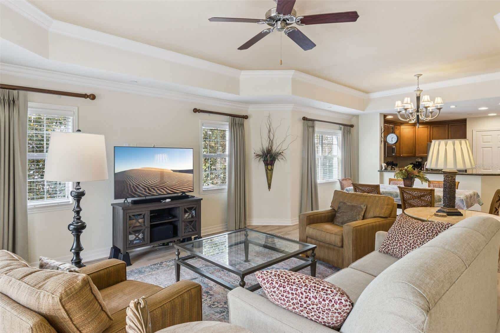 A spacious living room with a flat-screen TV, comfortable seating, a glass coffee table, and a ceiling fan.