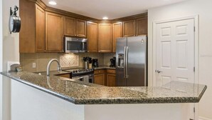 A kitchen with wooden cabinets, a stainless steel refrigerator, a microwave, a stove, and a sink. - New! Epic Reunion Family Retreat (Kissimmee)