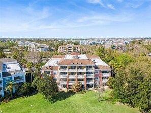 Um edifício residencial de vários andares com um pátio central, rodeado por vegetação e outros edifícios residenciais.