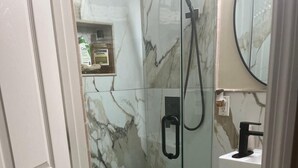 A bathroom with a glass-enclosed shower, marble walls, a white sink, and a mirror.