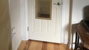 A white door with a mirror, a wooden floor, and a small table with a chair.