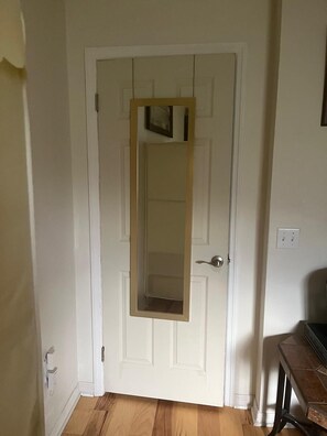 A white door with a mirror, a wooden floor, and a small table with a chair. - Clean & Cozy Room with Private Bath. Minutes to Disney. Free parking. (Kissimmee)